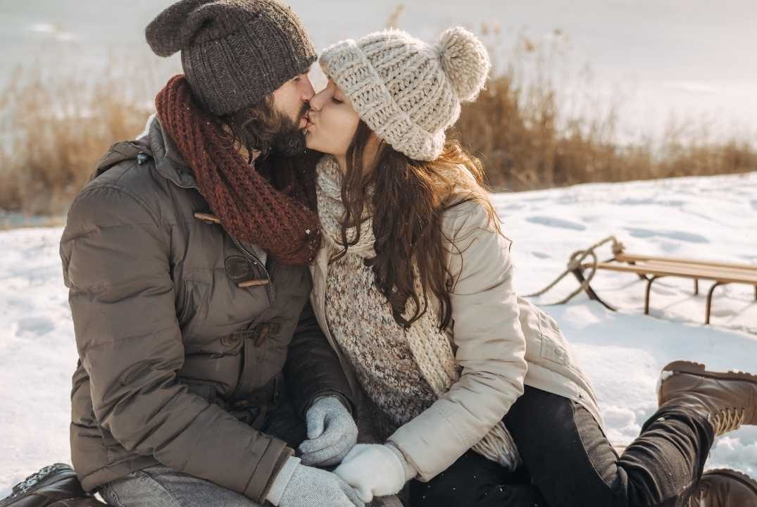 man kissing woman in snow with sled in the background.