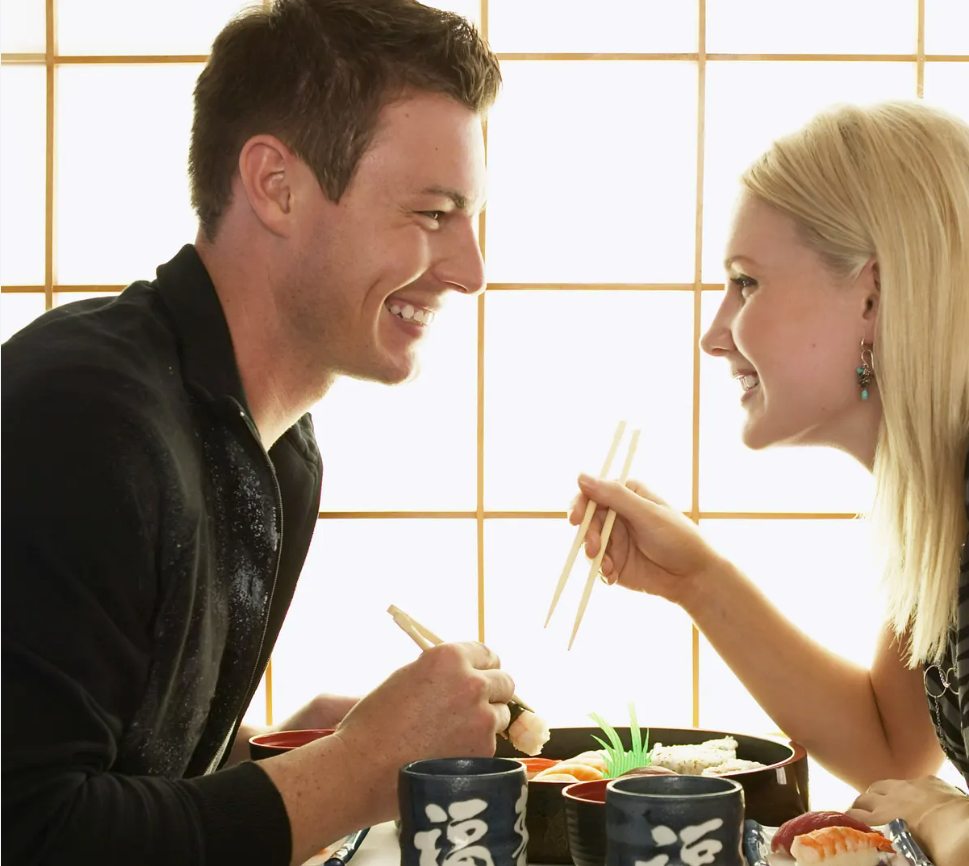 woman and man having sushi for dinner and laughing/ smiling at one another.