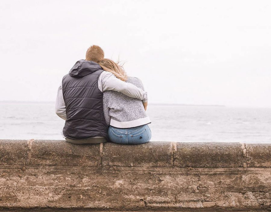 man and woman sitting on ledge overlooking the water.