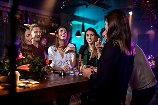 three women and two men crowded around at a table near a bar.