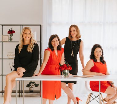 A group of five professional, working women behind a large white desk.