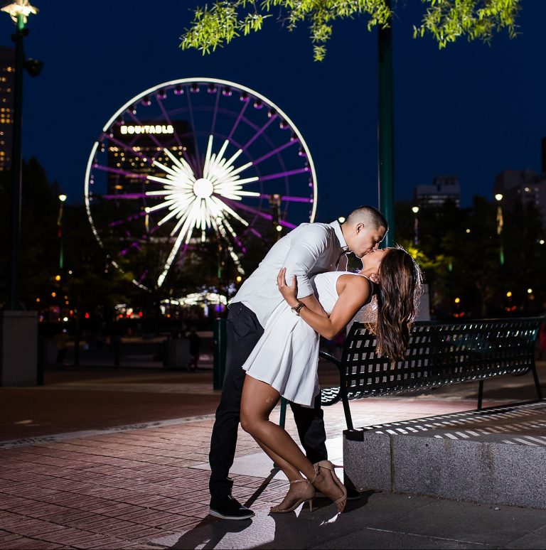 Boyfriend kissing girlfriend in front of ferris wheel.
