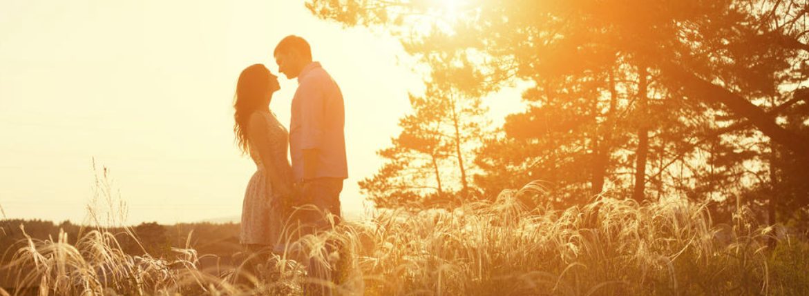 Couple looking at each other happily in the field with the sunset in the background.