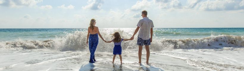 Mom, daughter, & the new husband holding hands at the beach in front of the waves.