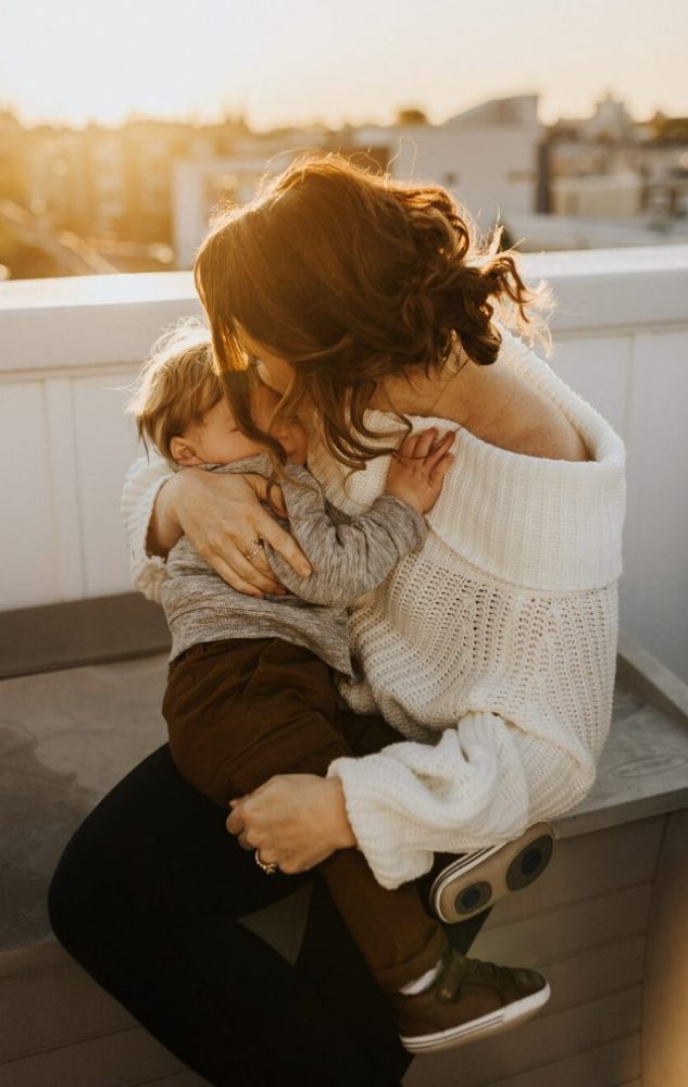 Mom holding son affectionately on the rooftop in front of a beautiful sunset. 