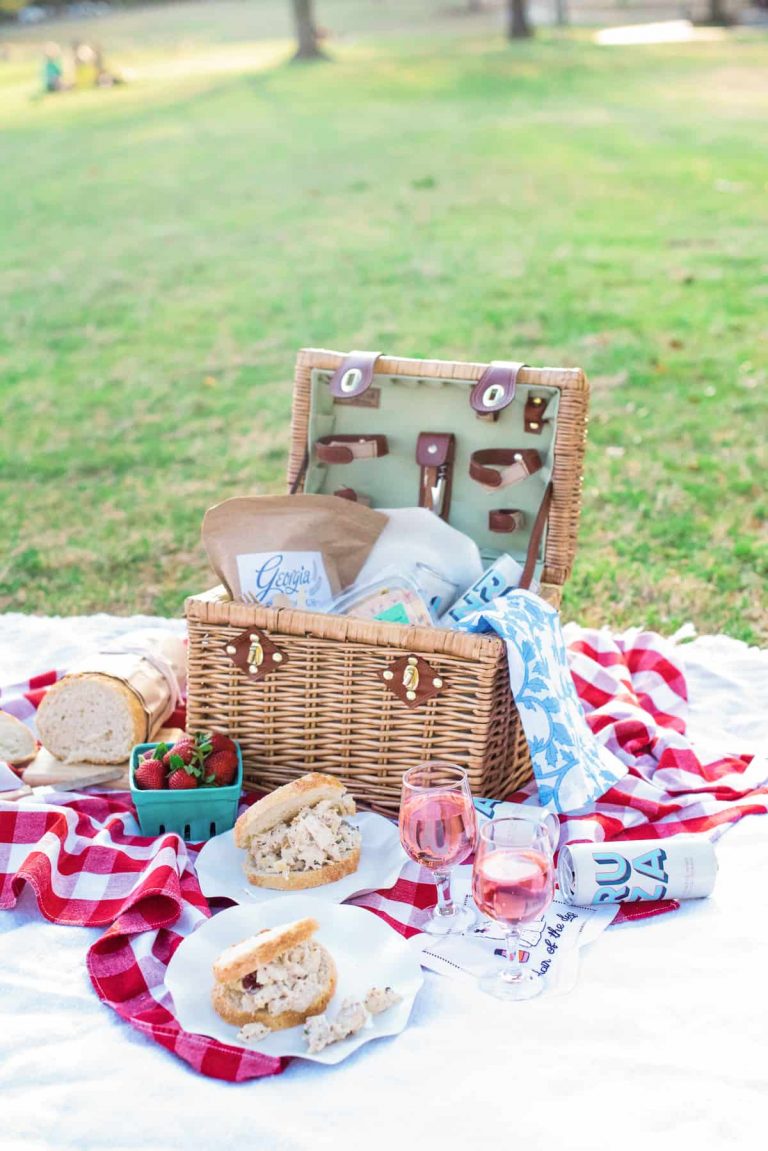 Open picnic basket with an array of sandwiches & drinks.