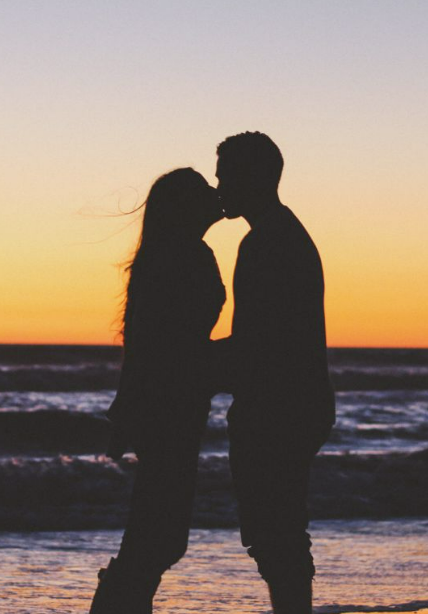 Couple kissing at the beach in front of the sunset. 