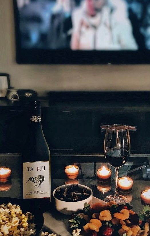 Cozy self-love night in with a bowl of popcorn, wine, & charcuterie board with a movie playing in the background.