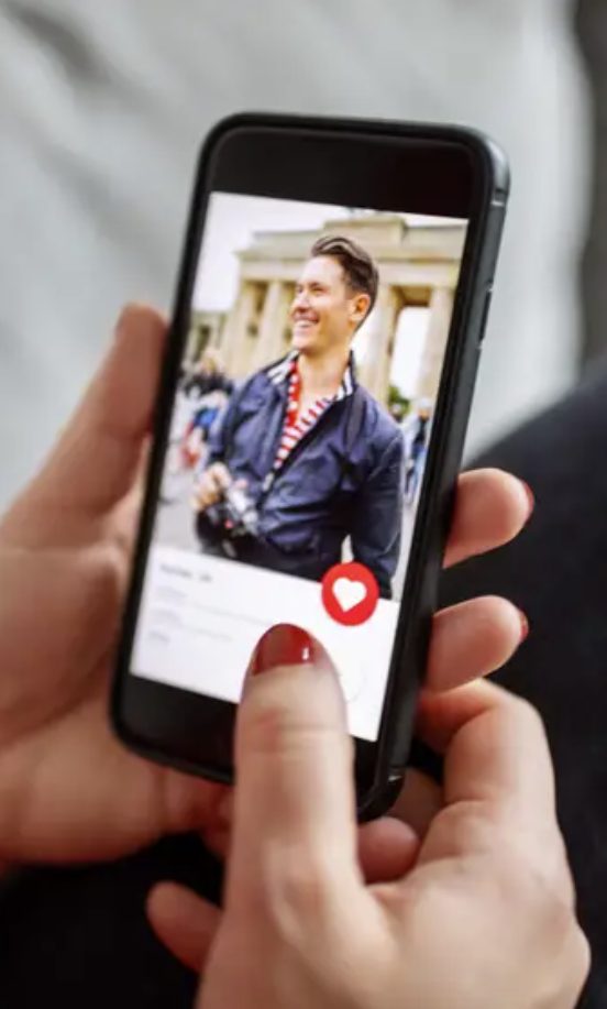 Woman holding iPhone with a dating app open, showing a man's online profile.