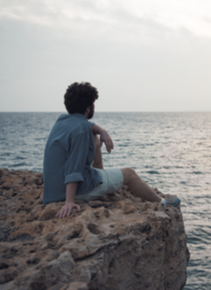 Man gazing out at the ocean while sitting on the edge of a cliff.