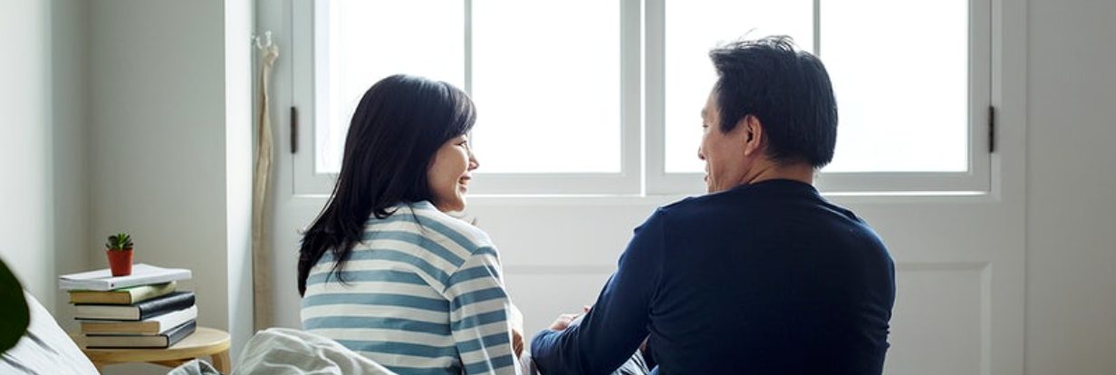 Couple sitting on the edge of bed in front of window discussing boundaries.