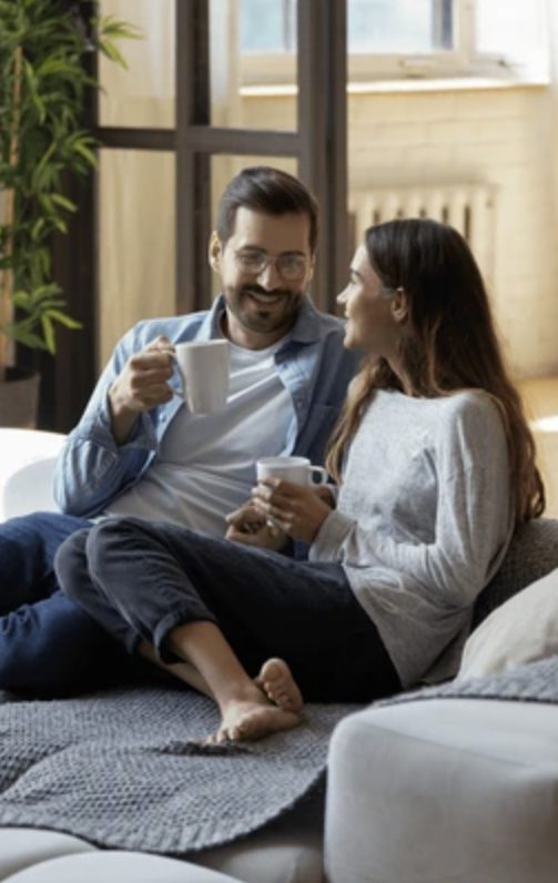 couple sitting on the couch holding cups of coffee talking about their boundaries.