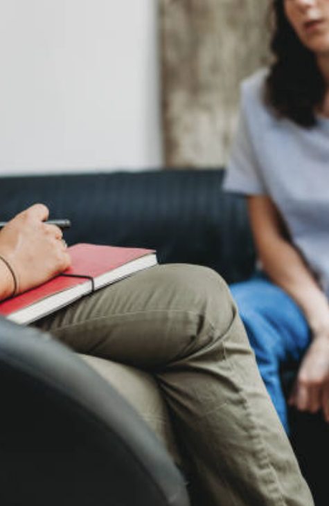 Woman sitting and talking to her therapist while she holds a red notebook in her lap.