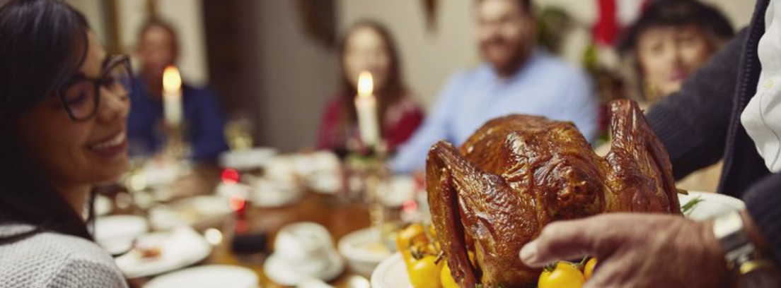 family gathered around the table, with someone about to place a plate of turkey on the table.