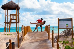 Couple at the beach, boyfriend is doing the "dip" with his girlfriend. The ocean is crystal blue in the background.