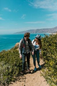 Couple hiking up the hill together with the crystal blue ocean in the background.