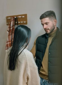Couple communicating in their apartment by the door. The man is talking to the woman.