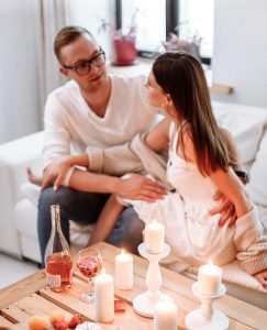 Couple talking on the couch with candles on the living room table. Man is holding woman lovingly.
