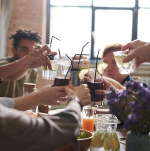 Group of people at dinner cheersing with their drinks while sitting at the table.
